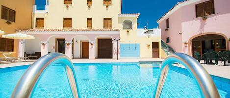 A swimming pool with a clear blue water surface, surrounded by buildings with balconies and windows.