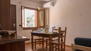 A dining area with a wooden table and chairs, a window with a view of trees, and an air conditioning unit on the wall.