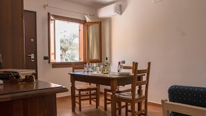 Een eetruimte met een houten tafel en stoelen, een raam met uitzicht op bomen, en een airconditioning op de muur.