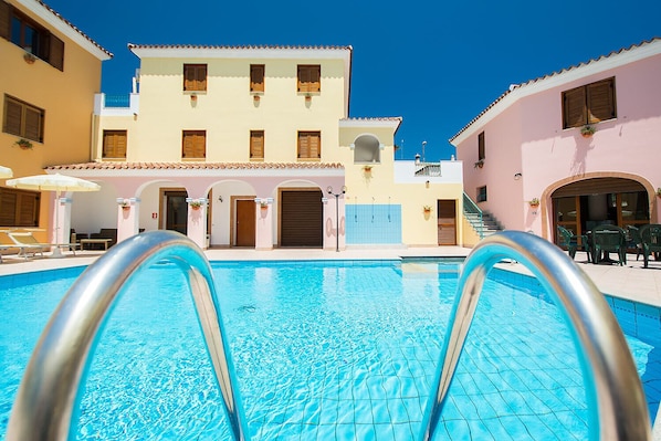 A swimming pool with a clear blue water surface, surrounded by buildings with balconies and windows.