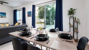 Un comedor moderno con una mesa de madera preparada para dos, un sofá gris y un ventanal de vidrio que da a un jardín.