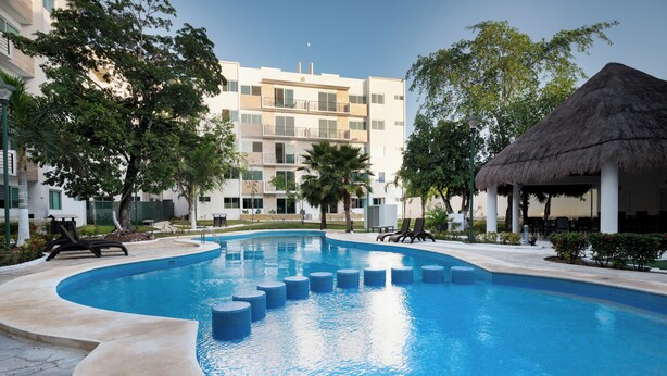 Una piscina de borde curvo, rodeada de sillas de descanso y un edificio con balcones.