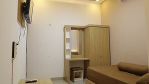 A compact bedroom with a bed, a wooden wardrobe, a small desk with a chair, and a mounted TV. - The Maguwo Premiere Kost Ekslusif (Depok)