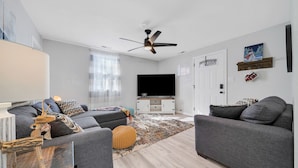 A modern living room with a grey sofa, a coffee table, a TV, and a ceiling fan. - A gem Right on Historic RTE 66 with outdoor space.  Walk to the action! (Williams)