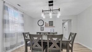 A dining area with a wooden table and chairs, a chandelier, a clock, and a window with curtains. - A gem Right on Historic RTE 66 with outdoor space.  Walk to the action! (Williams)