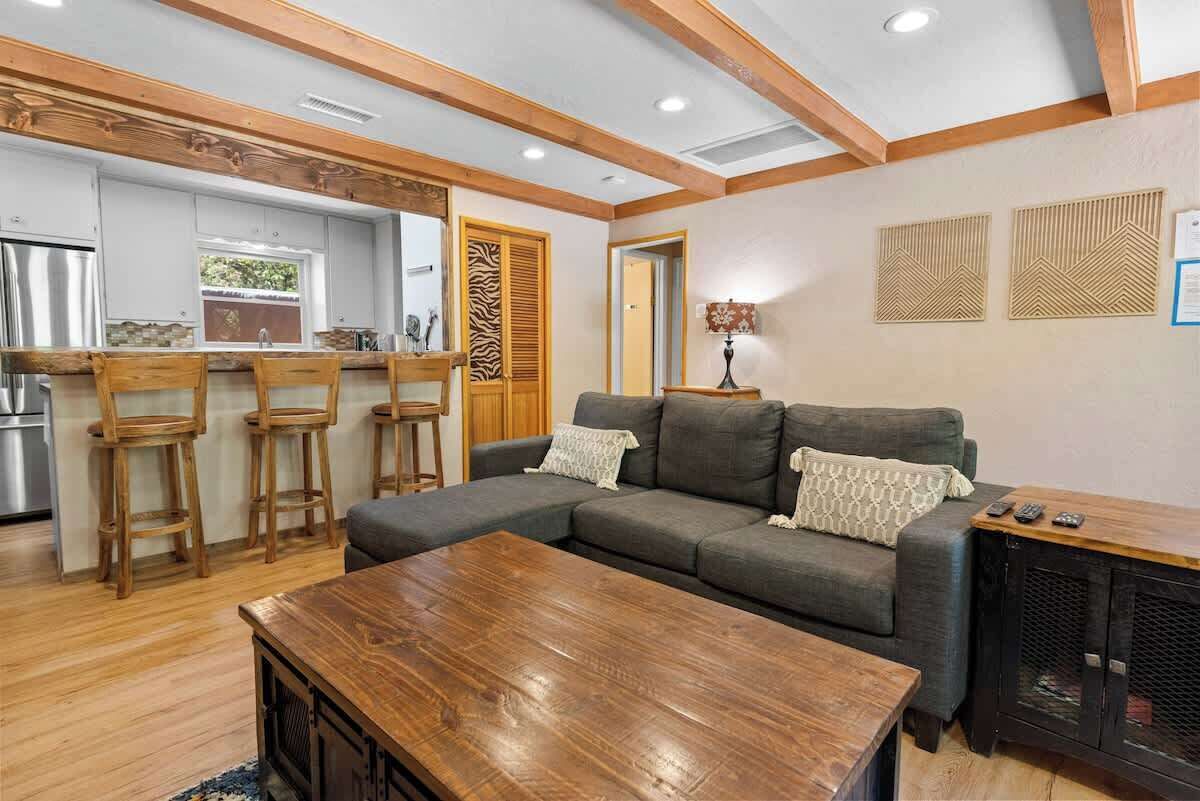 Una sala de estar moderna con un sofá seccional, taburetes de madera, una mesa de centro y un mueble para televisión.