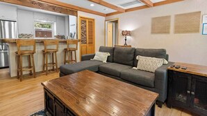 Een moderne woonkamer met een hoekbank, houten barstoelen, een salontafel en een tv-kast.
