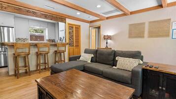 Una sala de estar moderna con un sofá seccional, taburetes de madera, una mesa de centro y un mueble para televisión.