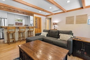 A modern living room with a sectional sofa, wooden bar stools, a coffee table, and a TV cabinet. - Serene Scene• Spa • Close to Bear Mtn (Big Bear Lake)