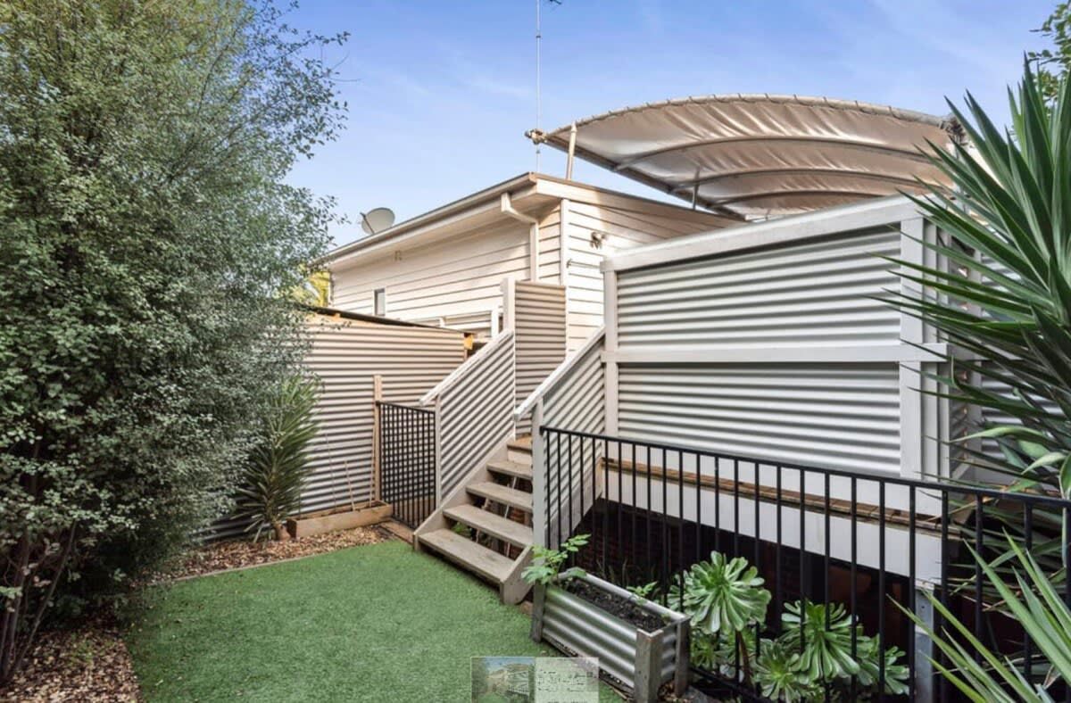 A residential property with a staircase leading to a covered porch, surrounded by a small lawn and potted plants.