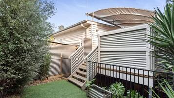 A residential property with a staircase leading to a covered porch, surrounded by a small lawn and potted plants.