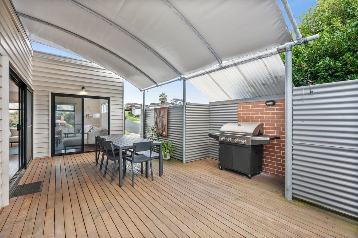 A covered patio area with a table and chairs, a grill, and a glass door leading to an indoor space.