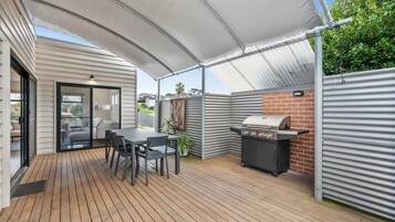 A covered patio area with a table and chairs, a grill, and a glass door leading to an indoor space.