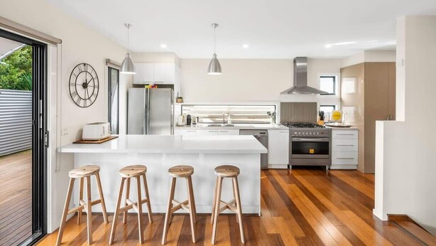 Una cocina moderna con una isla central, taburetes de bar, electrodomésticos de acero inoxidable y suelo de madera.