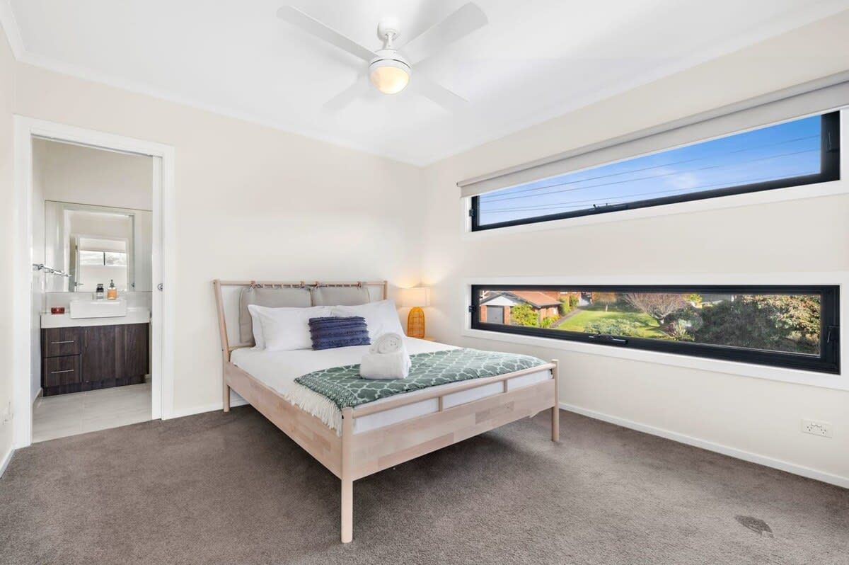 A bedroom with a bed, a ceiling fan, a window with a view, and a bathroom visible through an open door.