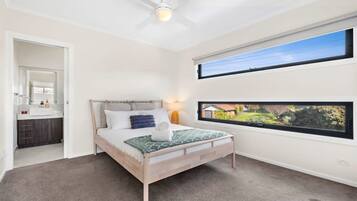 A bedroom with a bed, a ceiling fan, a window with a view, and a bathroom visible through an open door.