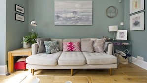 Ein Wohnzimmer mit einem hellen, modularen Sofa, einem Holztisch, einer Zimmerpflanze und einer Wandlampe.