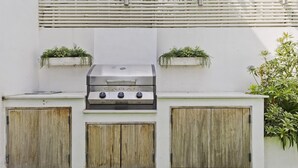 Eine moderne Außenküche mit integriertem Grill, Holzschränken und Topfpflanzen.