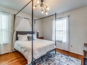 A four-poster bed with a white bedspread, a nightstand with a lamp, and a patterned rug.