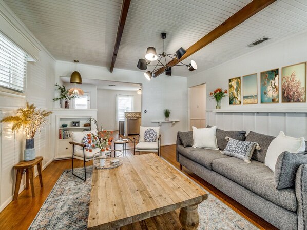 A spacious living room with a wooden coffee table, grey sofa, and a dining area with a wooden table.