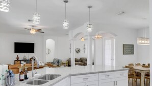 A modern kitchen with a large island, white cabinetry, and pendant lighting. - Sunny SW Cape Coral Getaway | Private Heated Pool, 4 Bedrooms & Modern Coastal Comfort (Cape Coral)