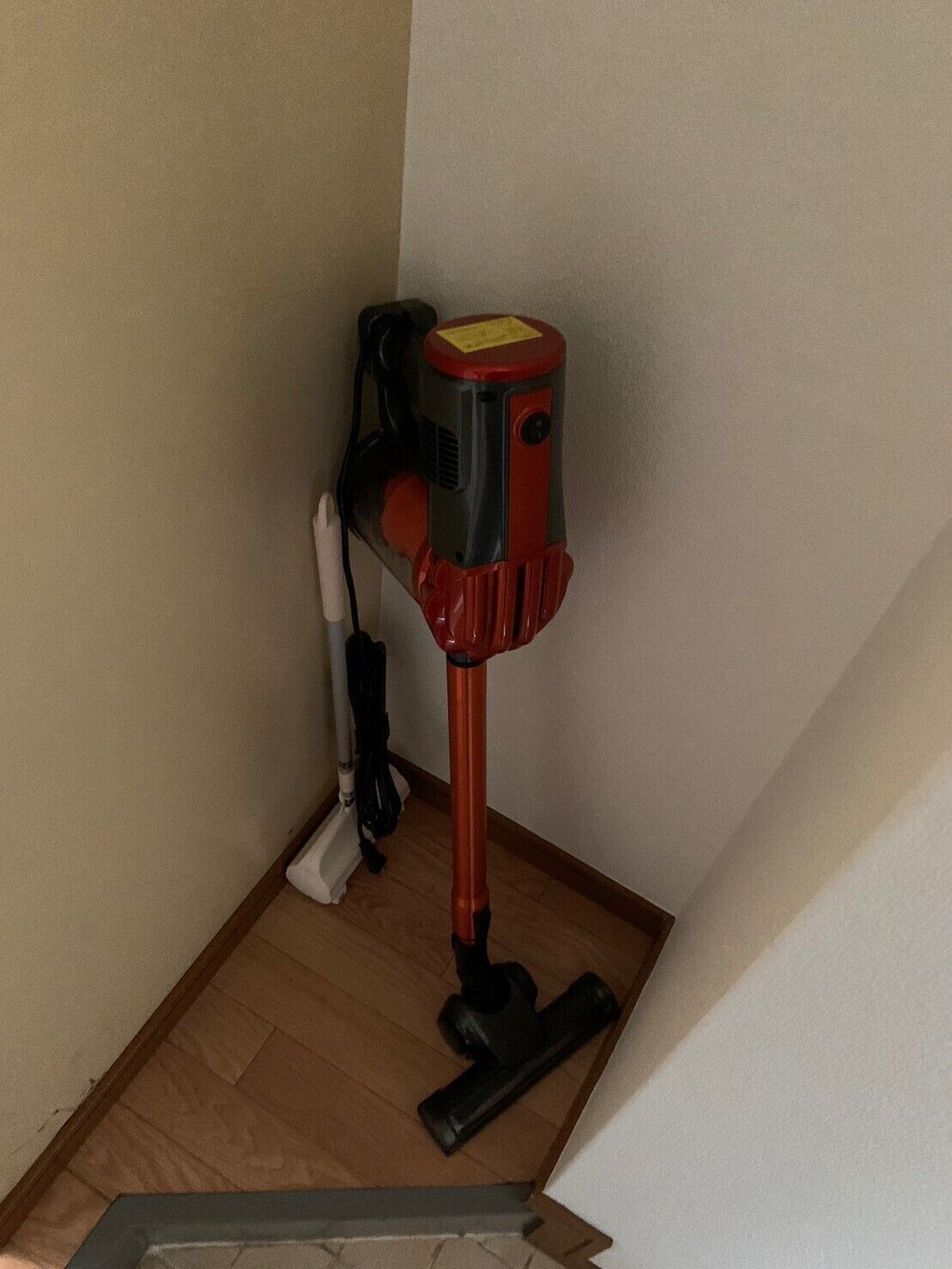 Een hoek van een kamer met een stofzuiger op de vloer en een stekkerdoos aan de muur.