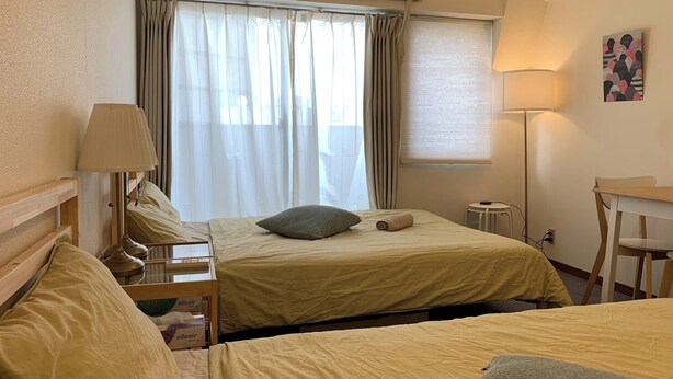 A hotel room with two beds, a desk, a lamp, and an air conditioning unit.