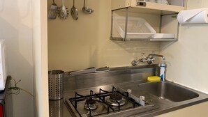 A kitchen with a gas stove, stainless steel sink, and hanging utensils.