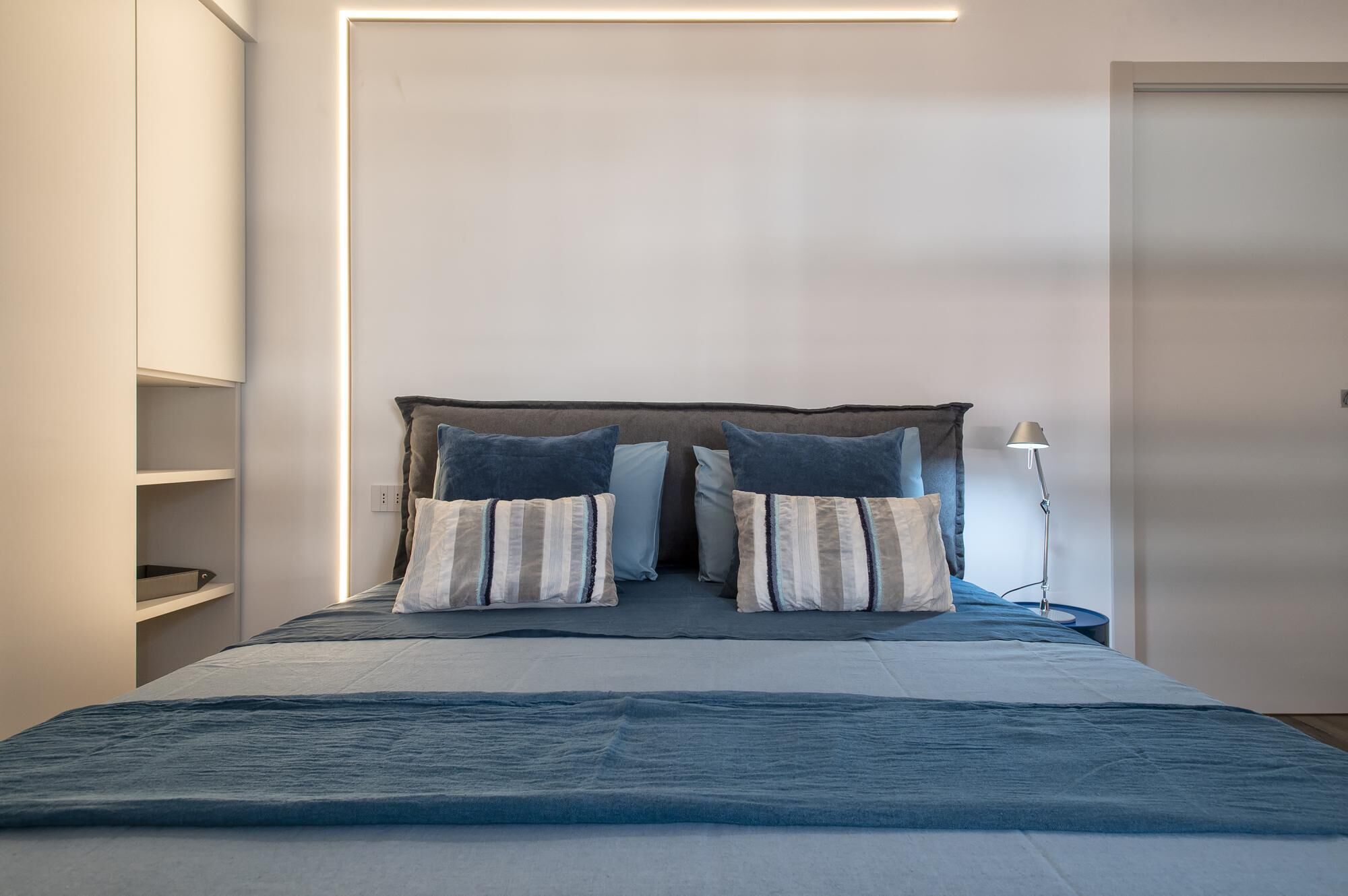 A modern bedroom with a bed, two pillows, a bedside lamp, and built-in shelves.