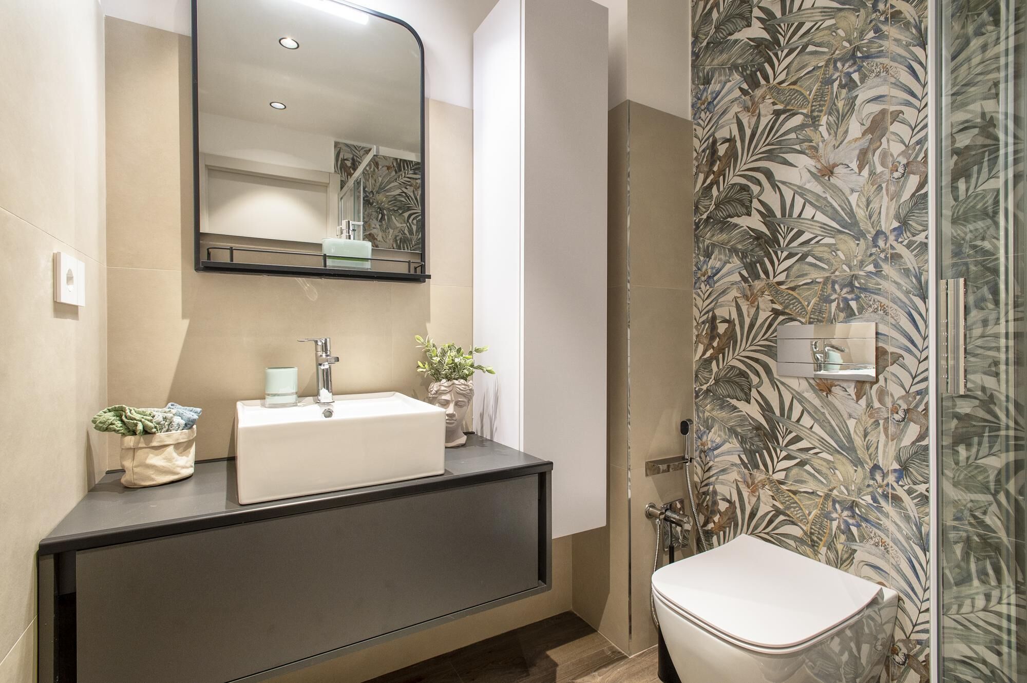 A modern bathroom with a white sink, a large mirror, and a shower with a floral wallpaper.