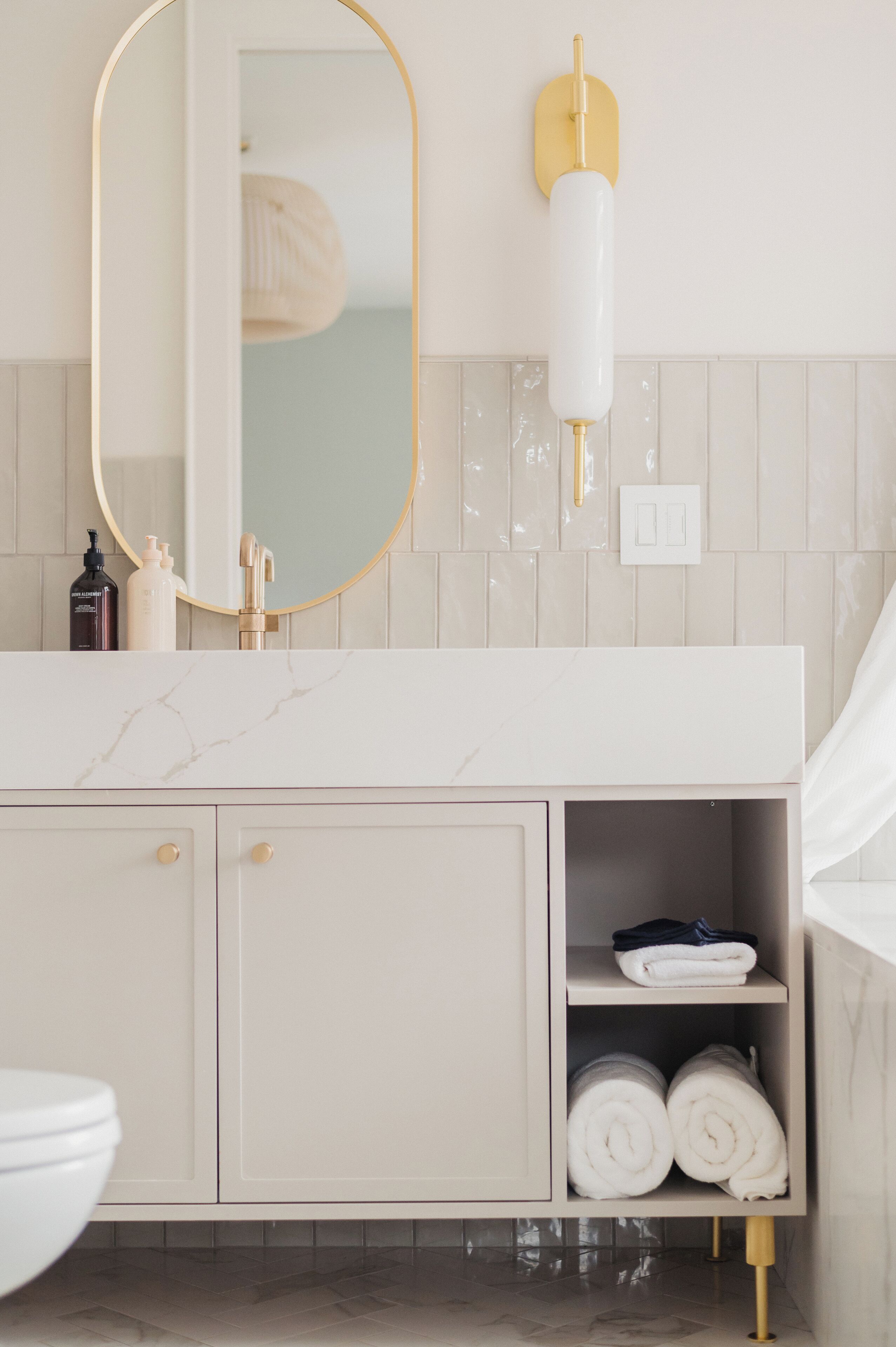 A bathroom with a white vanity, a gold-framed mirror, a towel shelf, and a toilet.