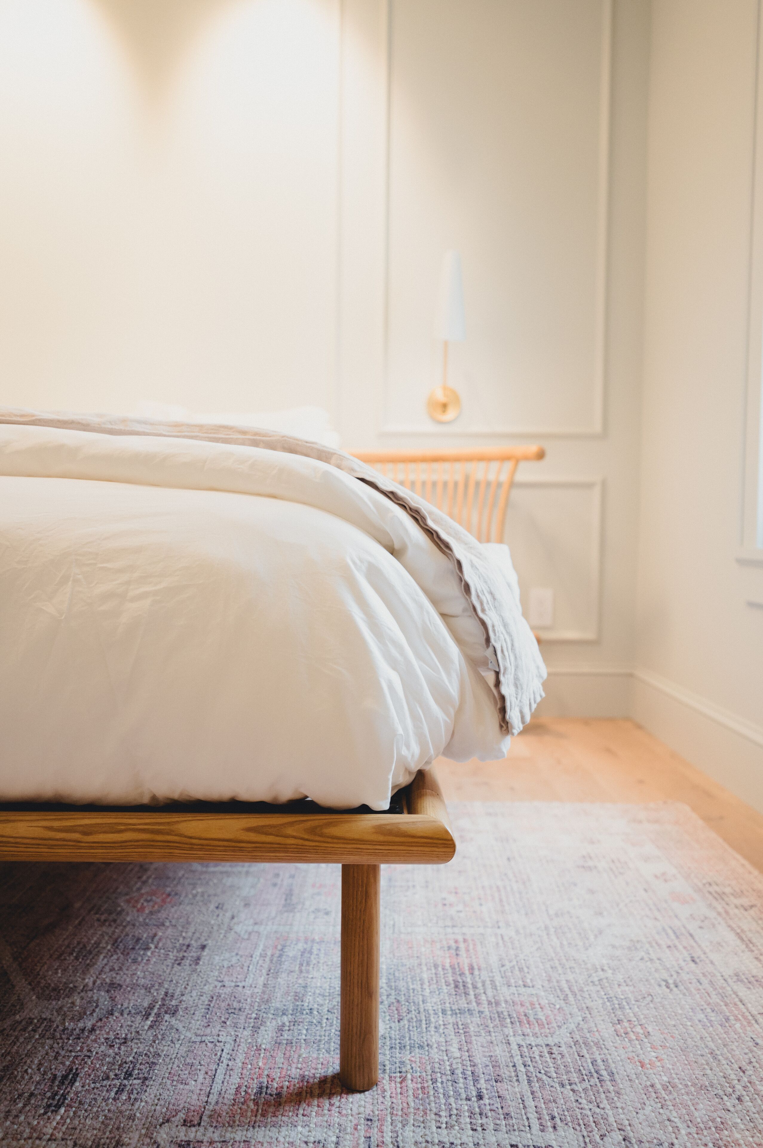 Una cama con estructura de madera y ropa de cama blanca en una habitación con alfombra estampada.
