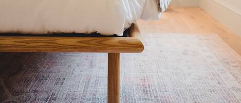 Una cama con estructura de madera y ropa de cama blanca en una habitación con alfombra estampada.