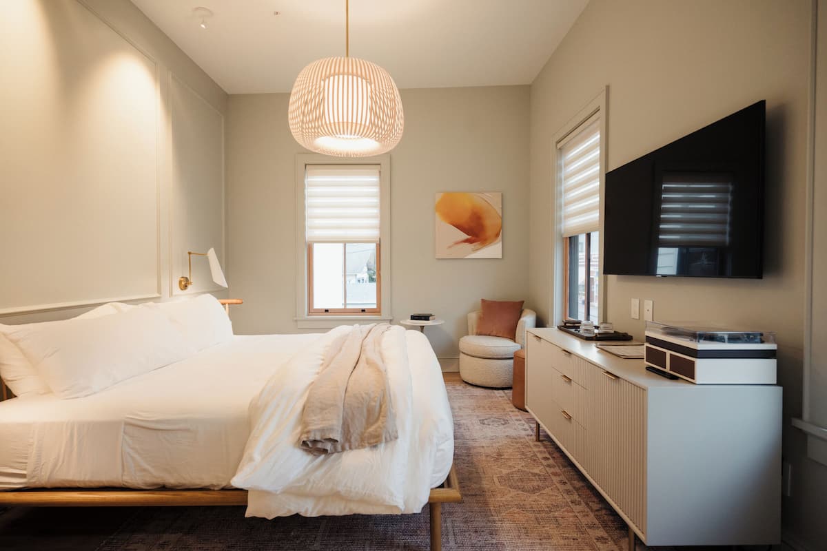 Un dormitorio moderno con cama, mesita de noche, lámpara y un televisor grande montado en la pared.