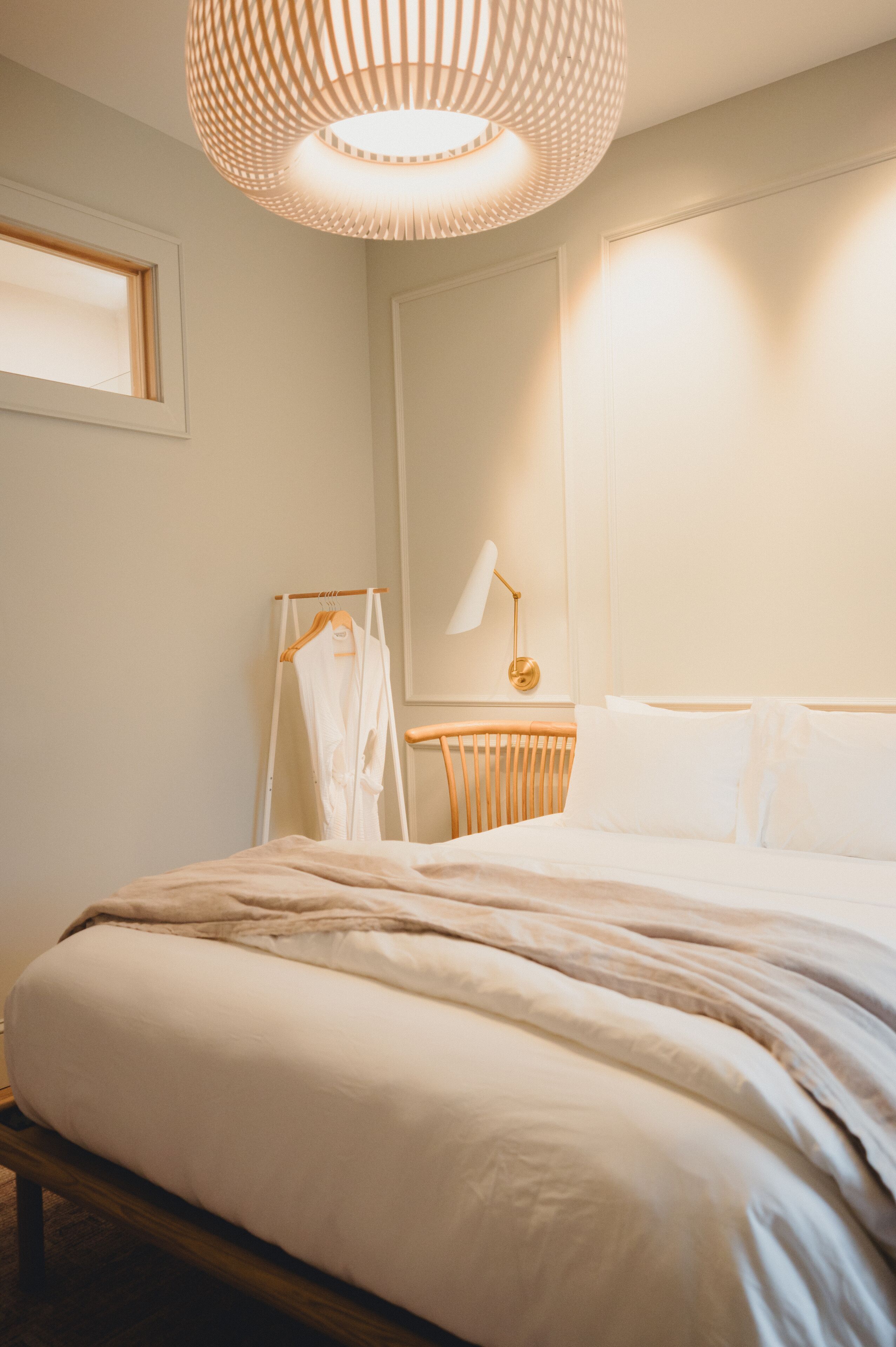 A bedroom with a bed, bedside table, lamp, and a hanging robe rack.