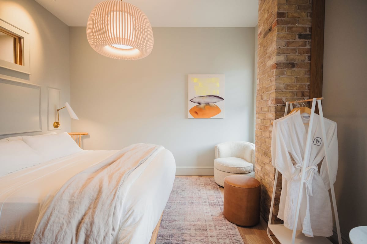 Un dormitorio moderno con una cama grande, una lámpara colgante, una silla y un perchero.