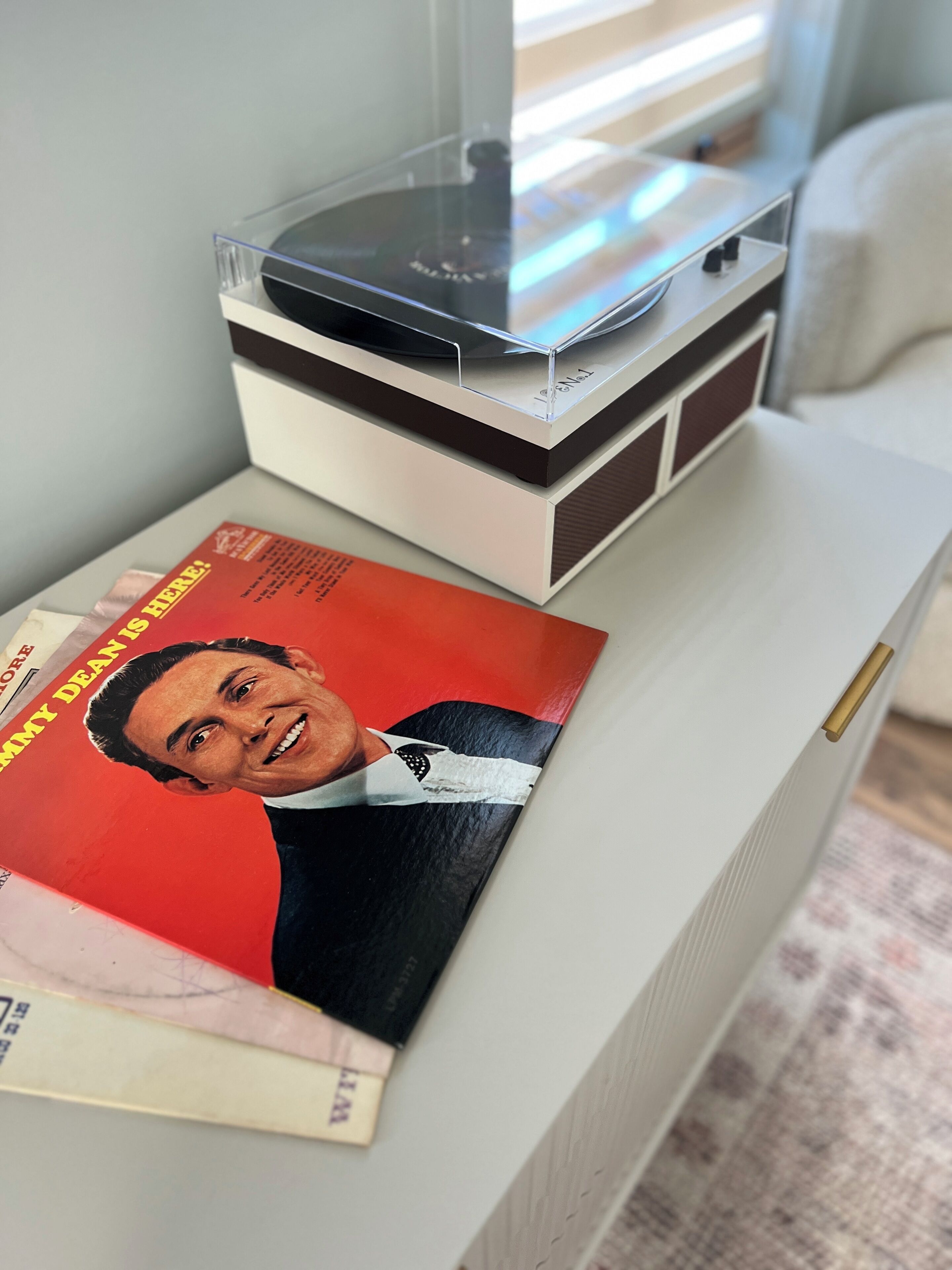 A vinyl record player on a white table with a magazine featuring a man in a suit.