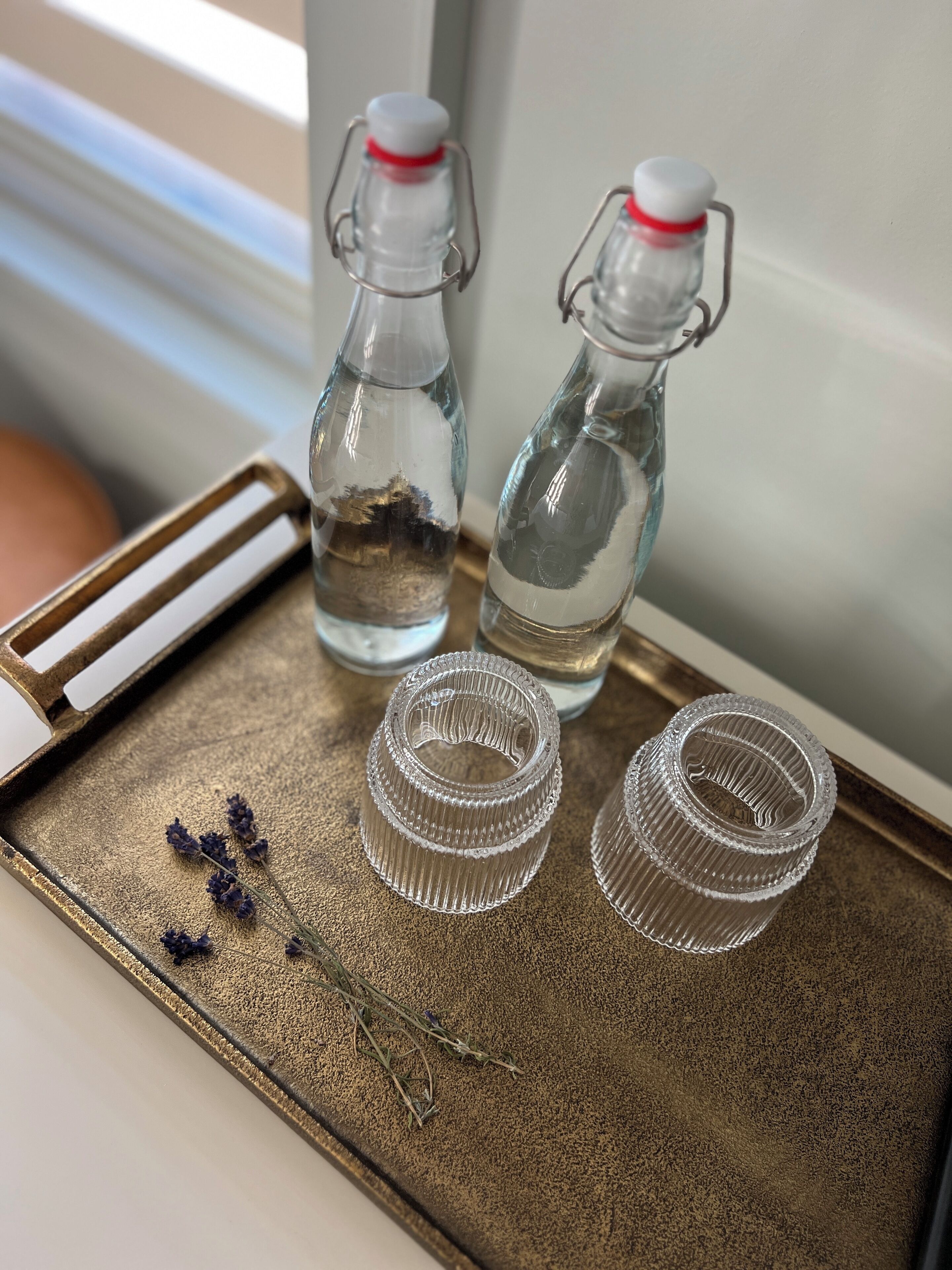 Two glass bottles with metal clasps and a tray with two empty glass containers and lavender sprigs.