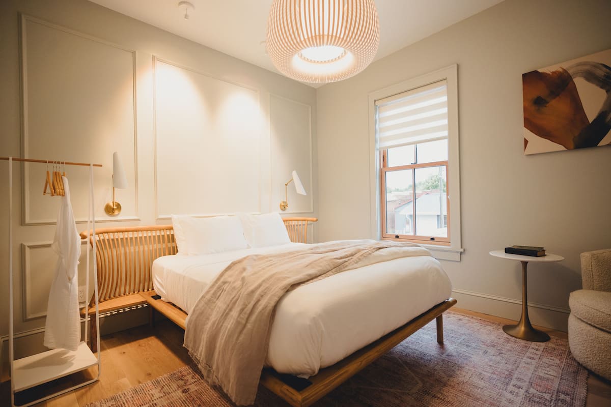 Un dormitorio con cama, un radiador, una ventana, una mesita y una silla.