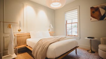 A bedroom with a bed, a radiator, a window, a small table, and a chair.