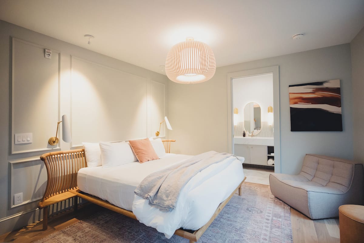 Un dormitorio moderno con una cama grande, mesitas de noche, una silla, un espejo y una lámpara colgante.