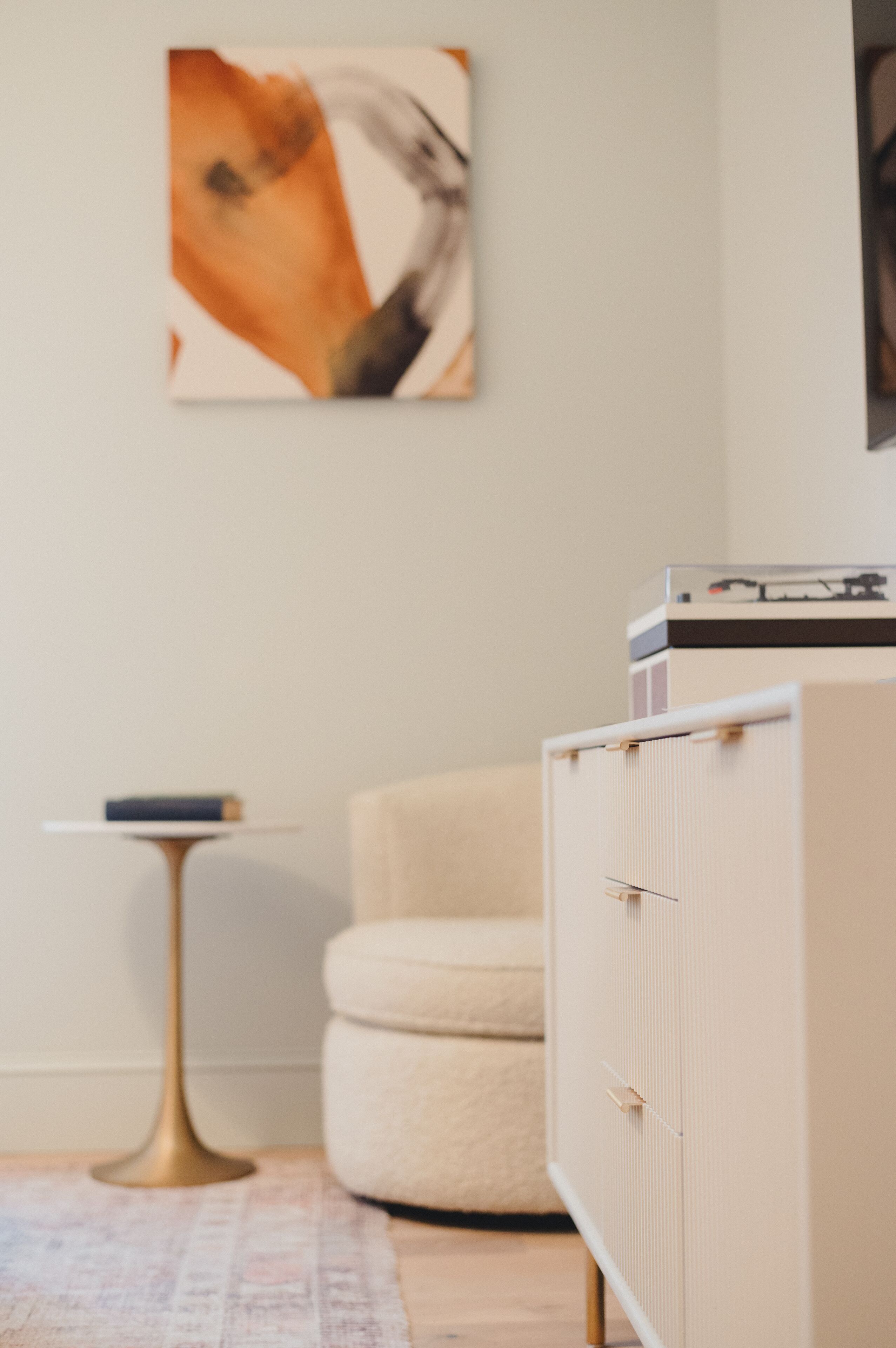 A room with a beige sofa, a small round table with a book, a floor lamp, and a cabinet with a record player.