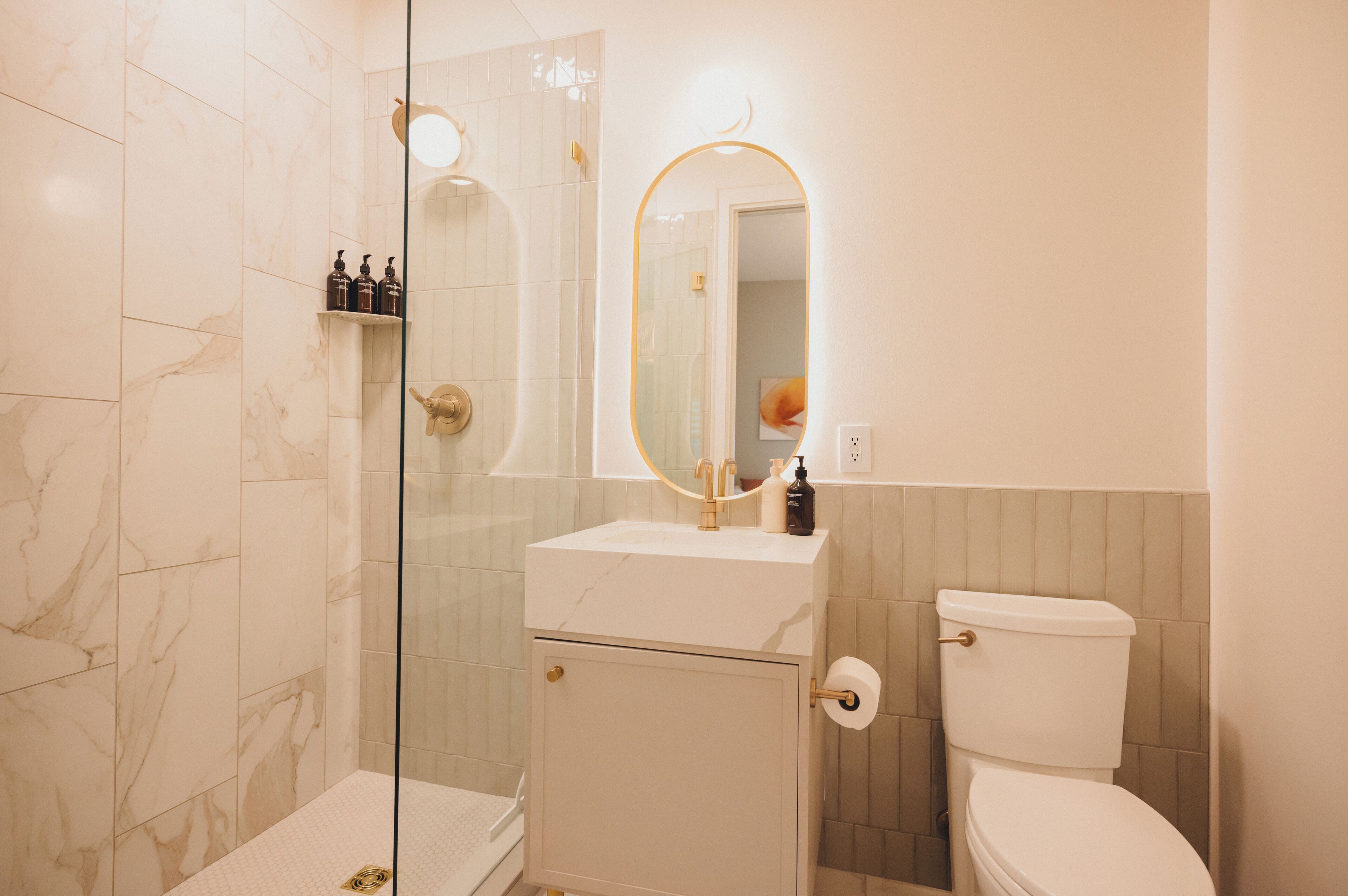 Un bagno con box doccia in vetro, un lavandino bianco con rubinetto dorato e un water con rivestimento a mosaico beige.