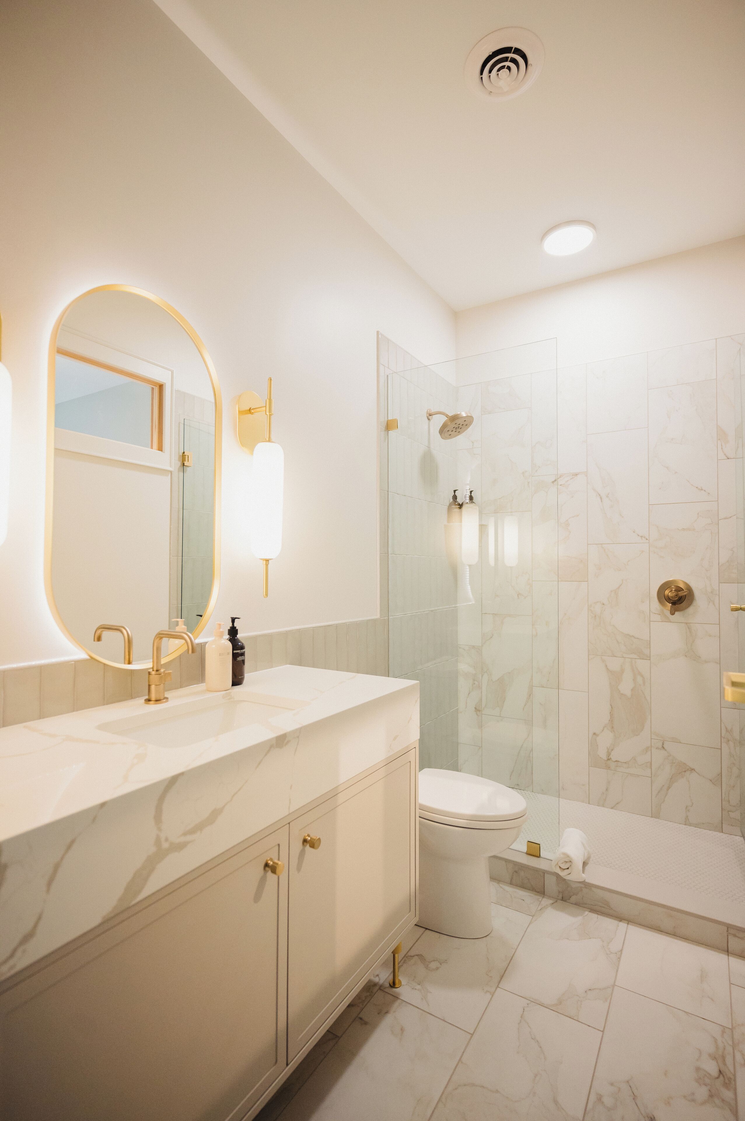 Un baño moderno con tocador de mármol, un espejo grande, inodoro y zona de ducha.