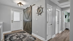 A hallway with a wooden door, a wall-mounted ship's wheel, and a ceiling light fixture. - Anchors Landing Waterfront Home | Dock | Foosball | Fire Pit | Close To The Beach | Dog Friendly (Palm Coast)