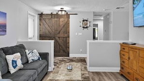 A living room with a gray sofa, wooden dresser, and a large barn door. - Anchors Landing Waterfront Home | Dock | Foosball | Fire Pit | Close To The Beach | Dog Friendly (Palm Coast)