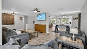 A spacious living area with a large sofa, a coffee table, a TV, and a kitchen in the background. - Anchors Landing Waterfront Home | Dock | Foosball | Fire Pit | Close To The Beach | Dog Friendly (Palm Coast)