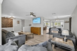 A spacious living area with a large sofa, a coffee table, a TV, and a kitchen in the background.