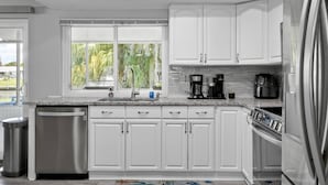 A modern kitchen with white cabinets, a dishwasher, a coffee maker, and a refrigerator. - Anchors Landing Waterfront Home | Dock | Foosball | Fire Pit | Close To The Beach | Dog Friendly (Palm Coast)