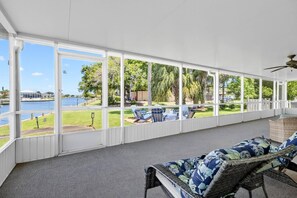 A covered outdoor area with a view of a body of water, a grassy lawn, and a lounge chair. - Anchors Landing Waterfront Home | Dock | Foosball | Fire Pit | Close To The Beach | Dog Friendly (Palm Coast)